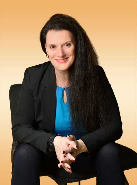 Cornelia Leclerc, Stresscoach, sitzt lächelnd, mit auf den Knien aufgestützten Ellenbogen und verschränkten Fingern auf einem Stuhl